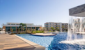 Piscina com cachoeira, espreguiçadeiras e um edifício moderno ao fundo.
