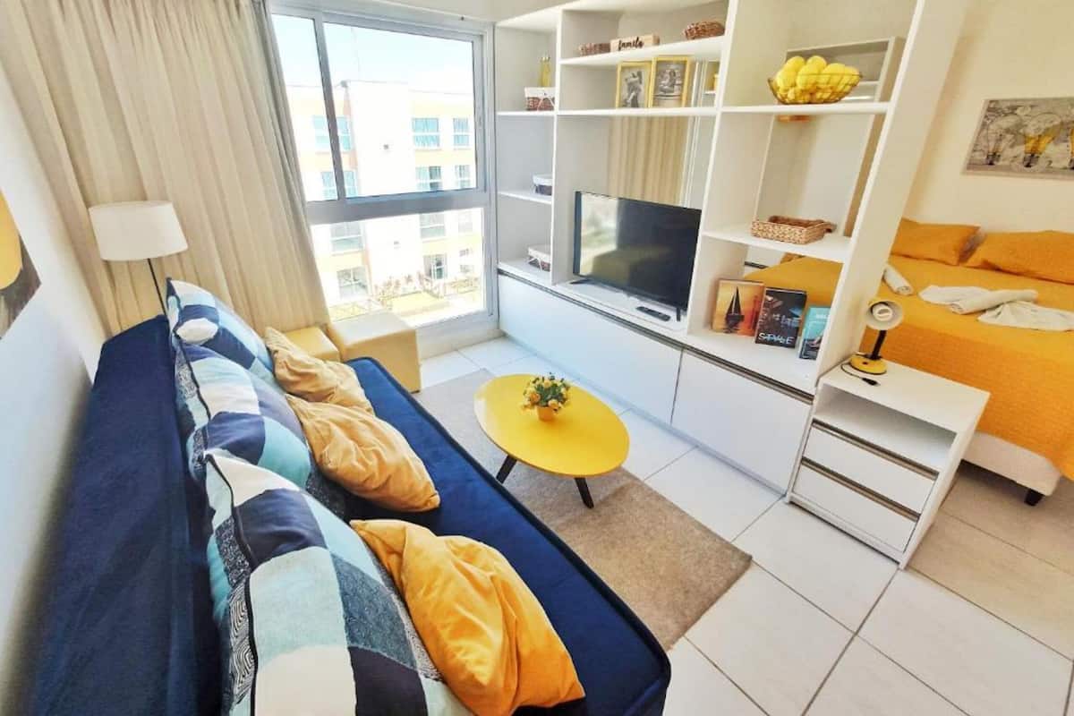 Un salon moderne avec un canapé, un téléviseur, une table basse jaune et une bibliothèque.