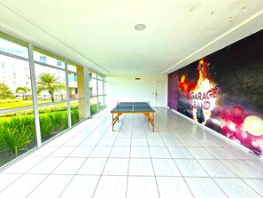 Un grand espace intérieur comprenant une table de ping-pong, de grandes fenêtres et une fresque murale.