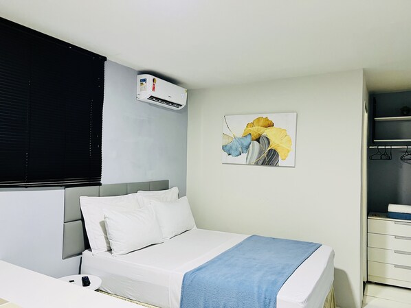 A hotel room with a bed, a bedside table, a wall-mounted air conditioner, a painting, and a wardrobe. - Edifício Creta (São Luís)