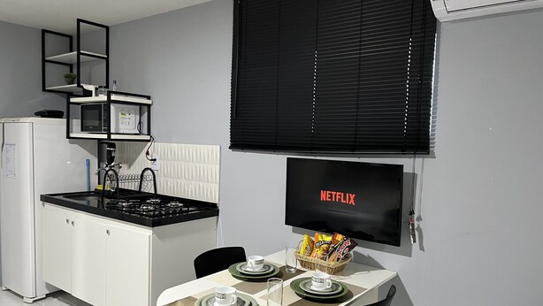 A compact kitchen with a microwave, stove, and a dining area with a table set for two. - Edifício Creta (São Luís)