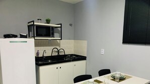 A compact kitchen with a microwave, sink, and stove. There is a dining table with plates and a glass. - Edifício Creta (São Luís)
