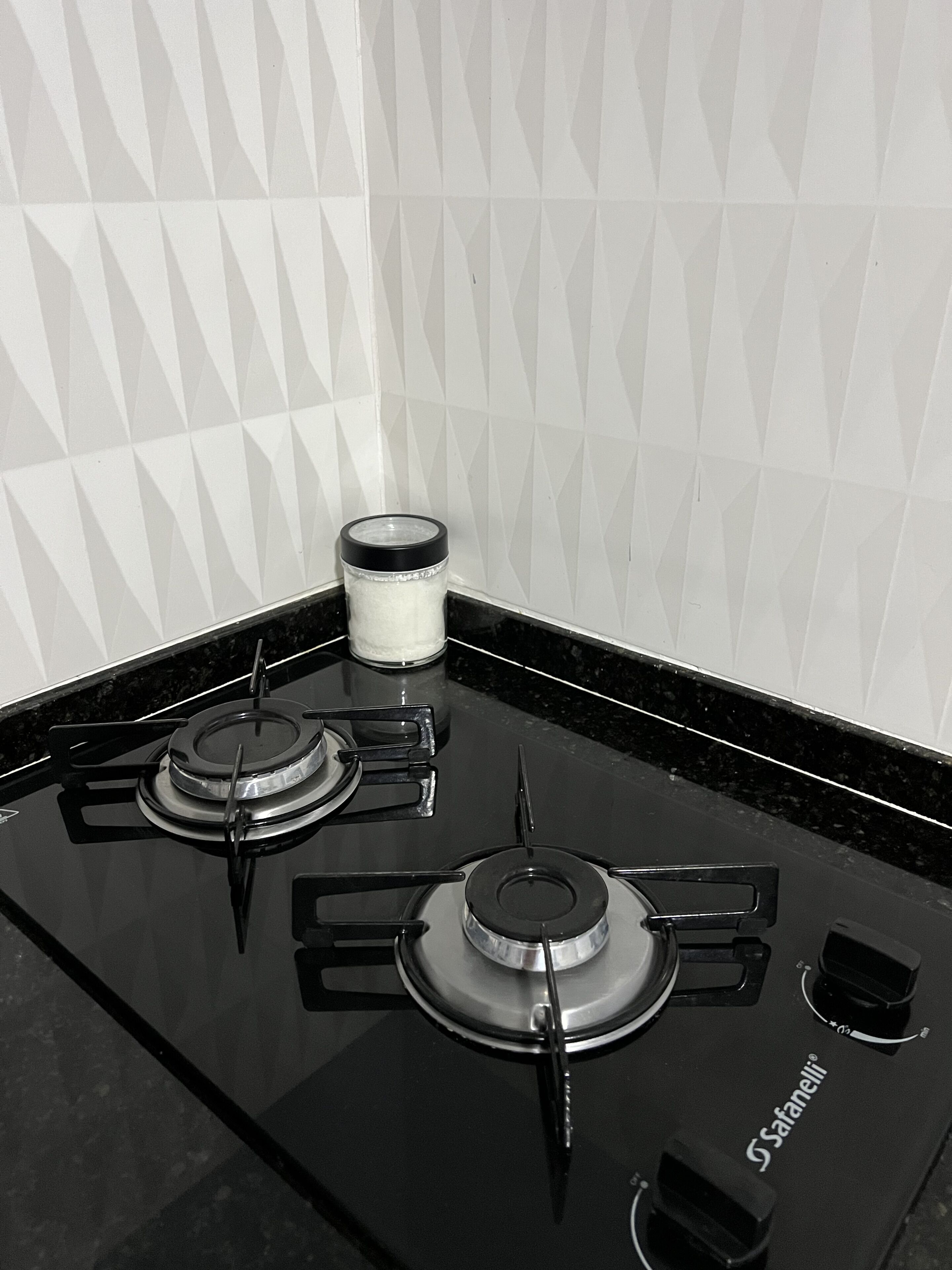 A black gas stove with four burners and a control knob, located in a kitchen with a black countertop and white tiled backsplash.