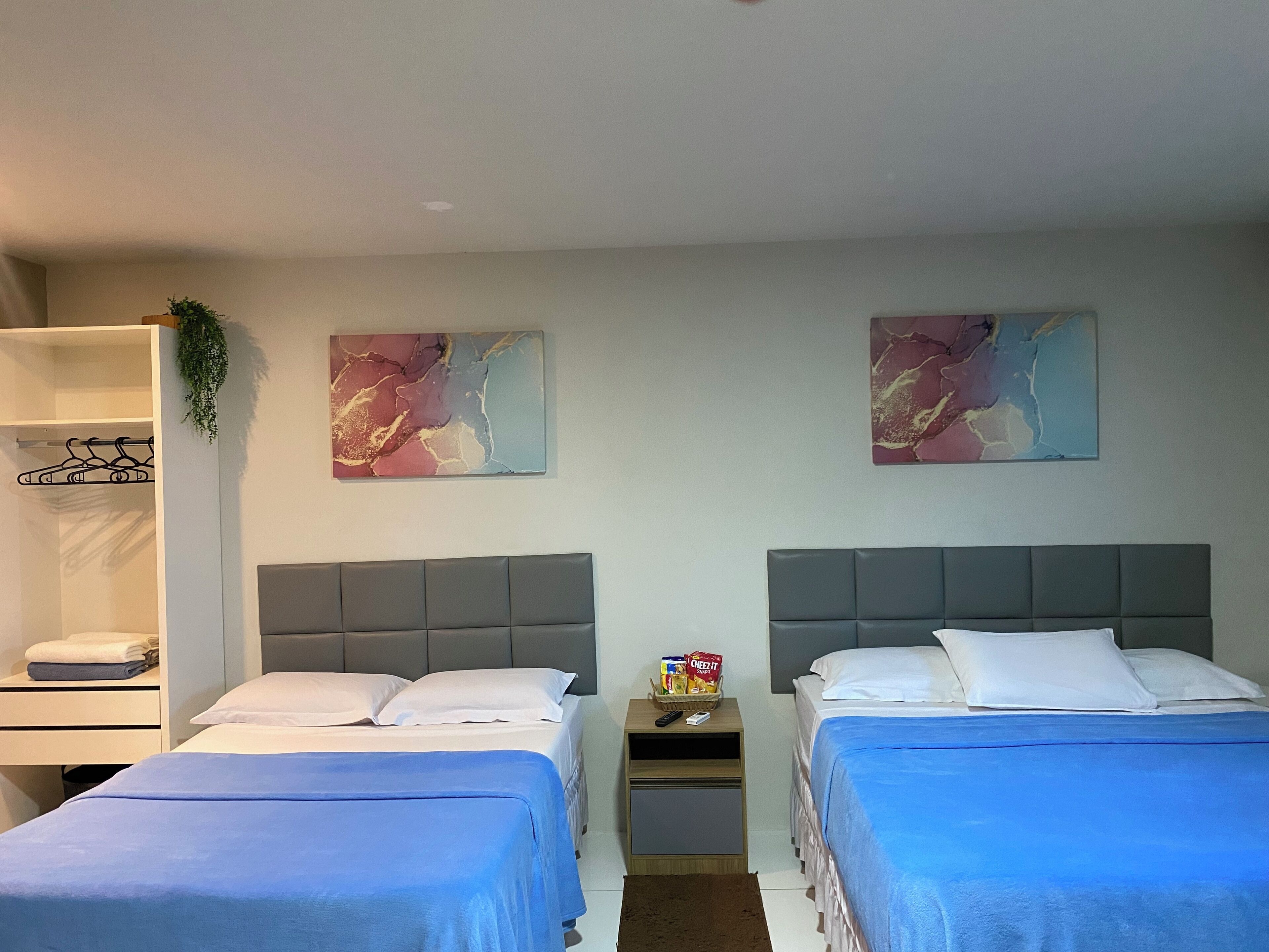 A hotel room with two beds, a wardrobe, and abstract art on the walls.