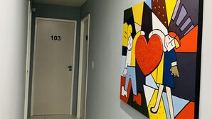 A hallway with a door labeled "103" and a colorful abstract painting on the wall. - Edifício Creta (São Luís)