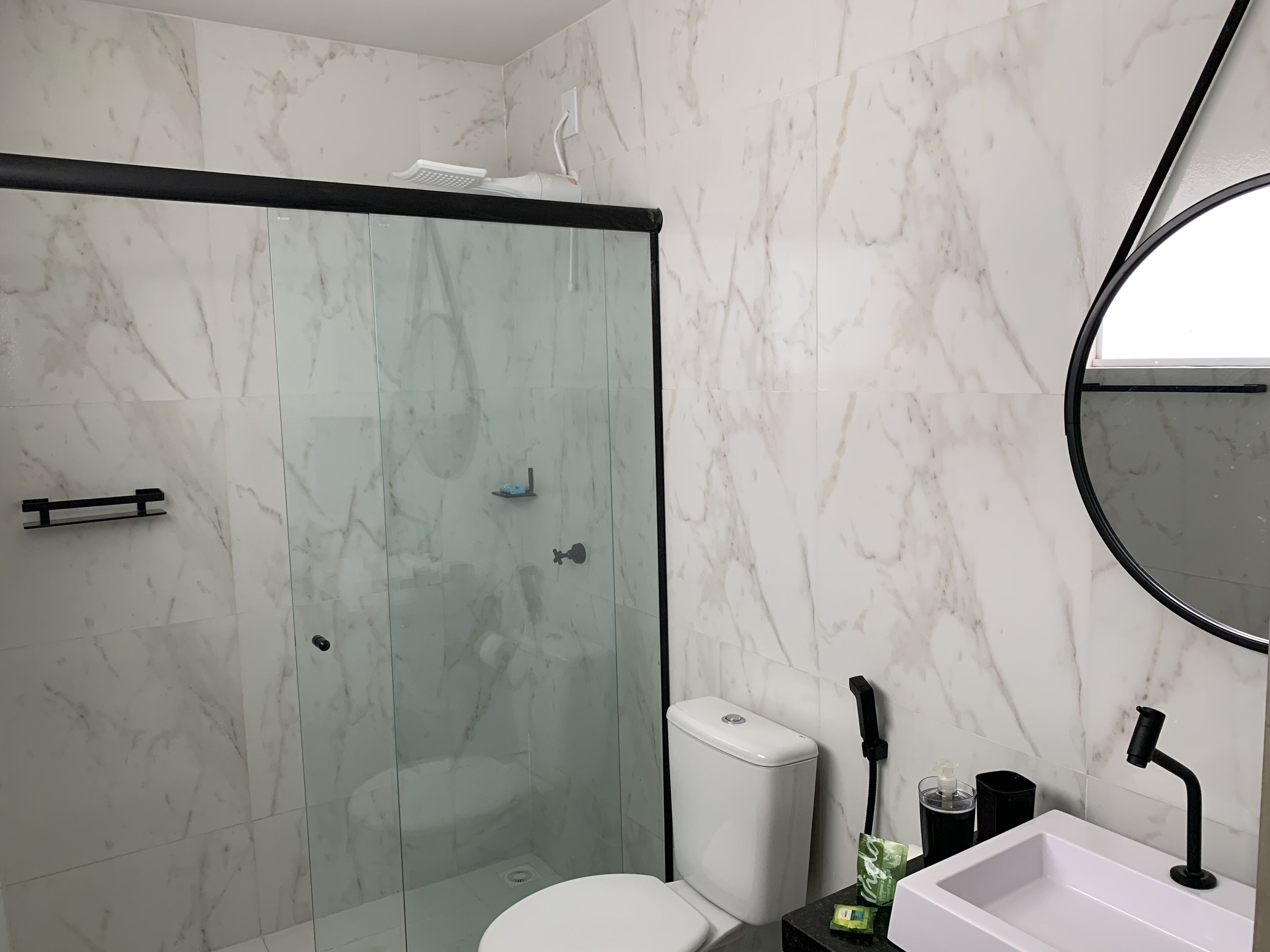 Un baño moderno con ducha de vidrio, inodoro y lavamanos con espejo.