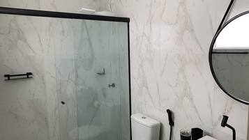 Un baño moderno con ducha de vidrio, inodoro y lavamanos con espejo.