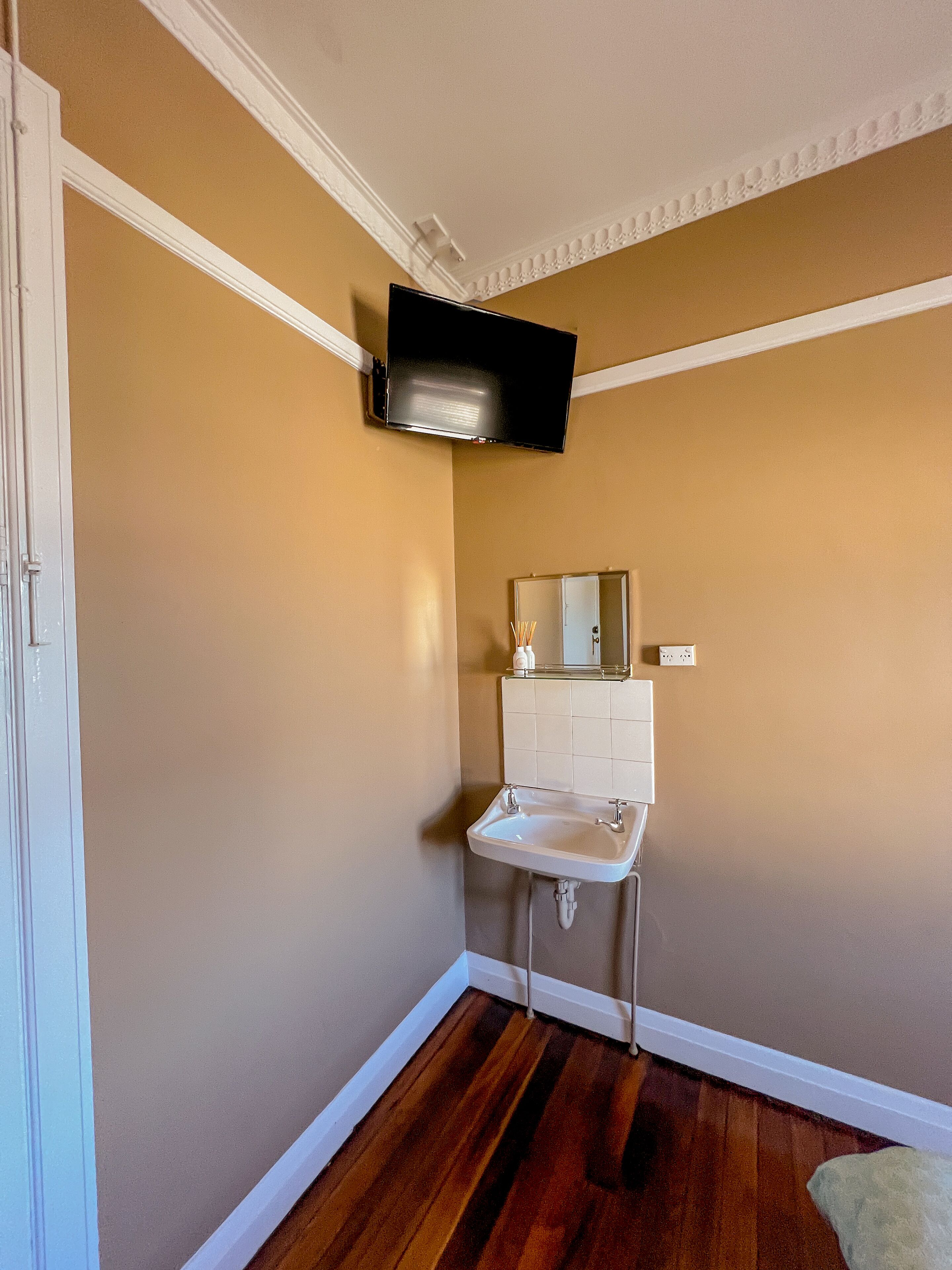 A bathroom with a white sink, a mirror above it, and a television mounted on the wall.