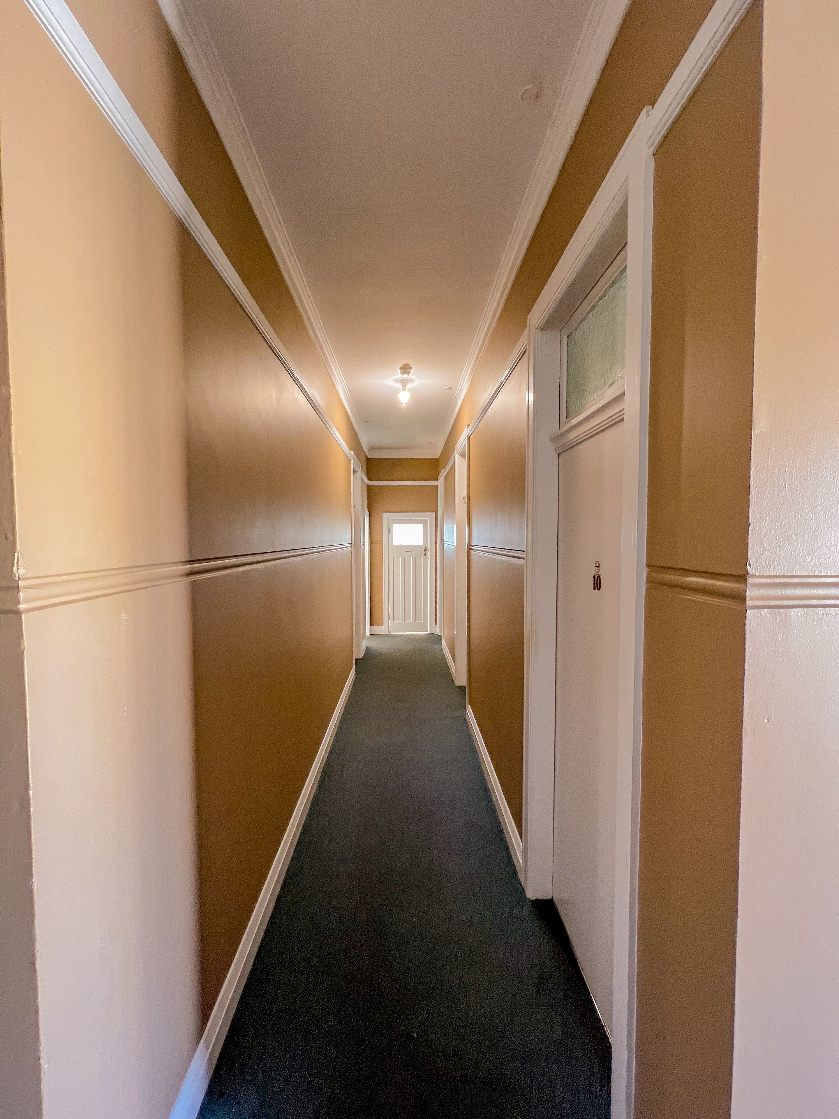 A long, narrow hallway with beige walls and a dark carpet.