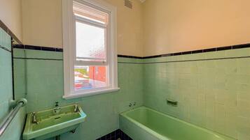 A bathroom with a green sink, a bathtub, and a window with blinds.