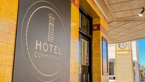 Entrada de un hotel con un cartel que dice 'HOTEL COMMERCIAL' y un reloj al fondo.