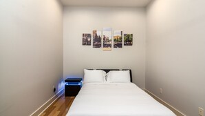 A bedroom with a bed, a nightstand with a blue light, and three framed pictures on the wall.