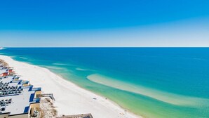 Eine Vogelperspektive zeigt einen Strand mit einer Reihe von Gebäuden entlang der Küste, einen klaren blauen Himmel und ruhige See.