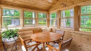 A wooden interior with a round table and chairs, large windows, and a ceiling fan. - Adorable Northwoods cabin (Iron River)