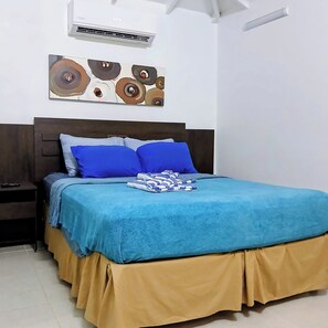 Une chambre à coucher comprenant un lit, une table de chevet, un climatiseur mural et un élément décoratif fixé au mur.
