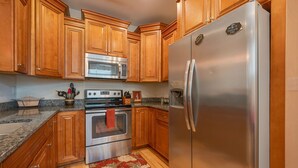 A kitchen with wooden cabinets, stainless steel appliances, granite countertops, and a red towel hanging on the oven. - Two Classy Homes - Sleeps 20, Steps from the Beach (Hampton)