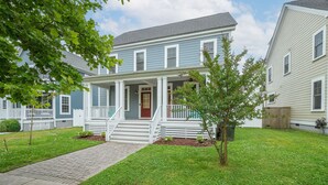 A two-story house with a front porch, a small tree, and a brick pathway leading to the door. - Two Classy Homes - Sleeps 20, Steps from the Beach (Hampton)