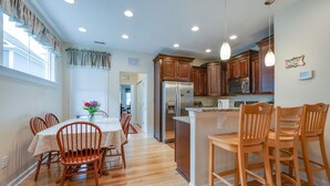 A modern kitchen with wooden cabinets, a stainless steel refrigerator, and a dining area with wooden chairs and a table. - Two Classy Homes - Sleeps 20, Steps from the Beach (Hampton)