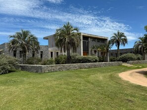 Un edificio moderno con fachada de piedra, rodeado de césped cuidado y palmeras.