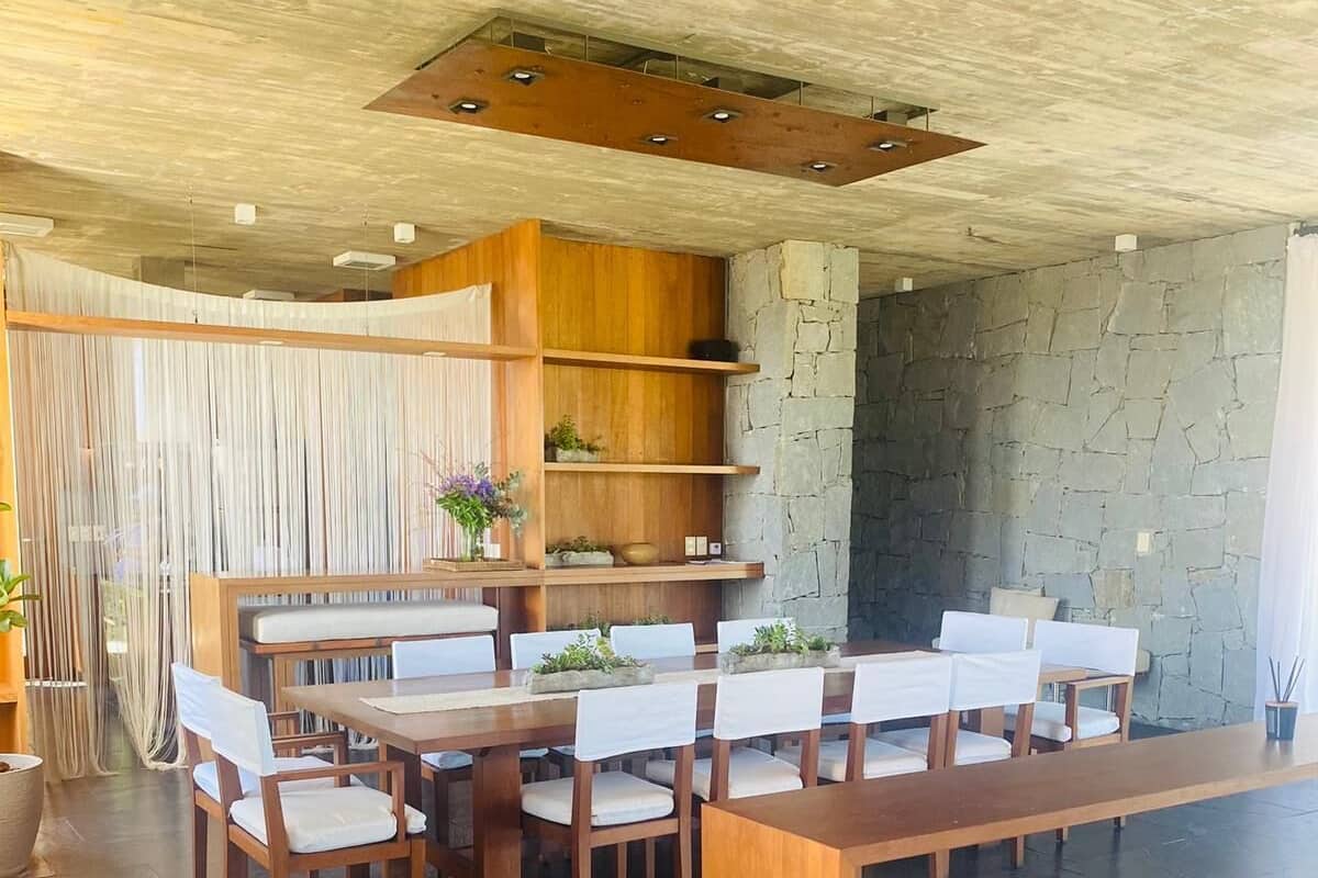 Uma sala de jantar moderna com uma longa mesa de madeira e cadeiras brancas, uma parede de pedra e um painel de madeira com prateleiras.