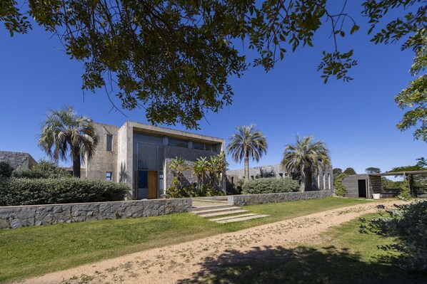 Una casa moderna con pared de piedra, palmeras y un cielo azul despejado.