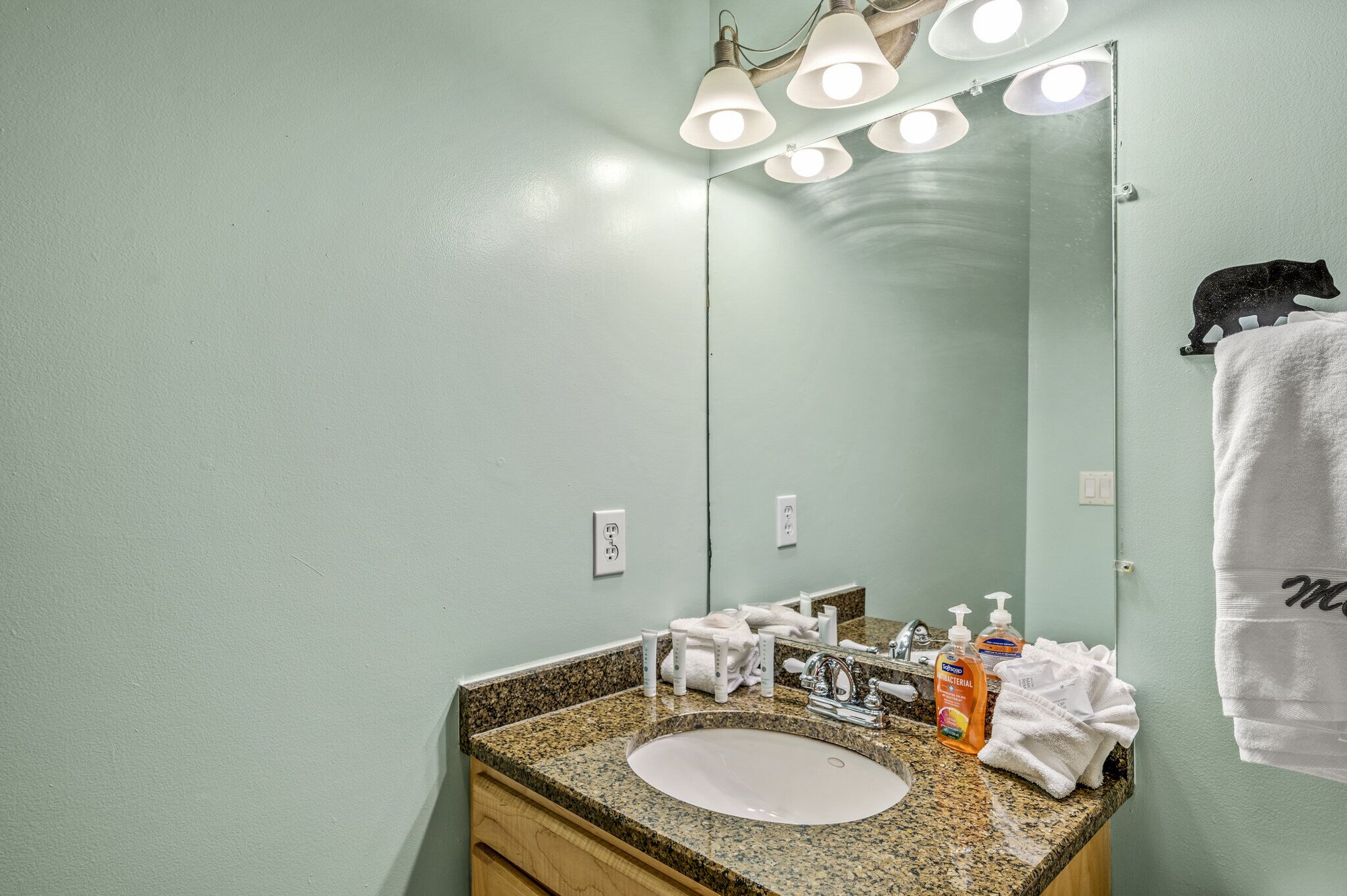 A bathroom with a granite countertop, a white sink, and a mirror. There are toiletries on the counter, and a towel rack with a towel hanging on it.