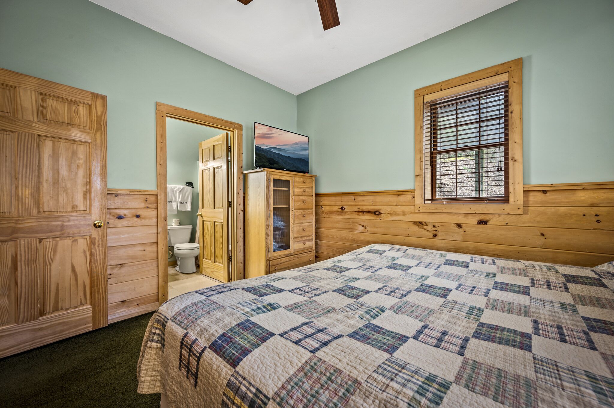 Une chambre à coucher avec une tête de lit en bois, une couvre-lit matelassé, une fenêtre avec des stores et une armoire en bois.