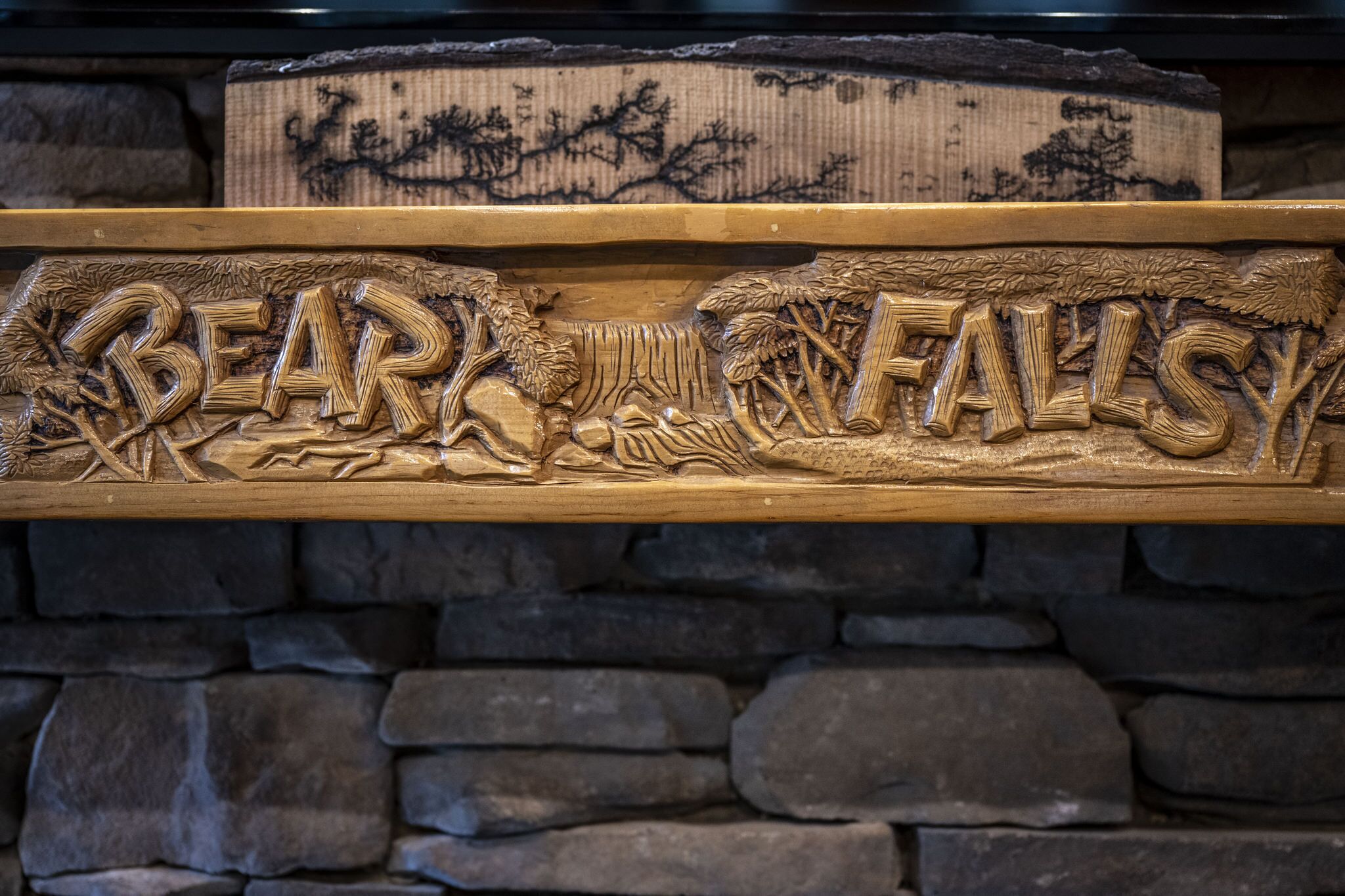 Un cartello di legno intagliato con il testo "BEAR FALLS" e un'illustrazione di un orso.