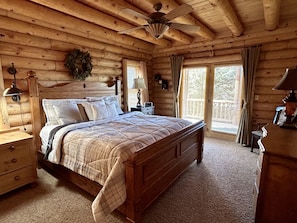 Un dormitorio de cabaña de madera con una cama, mesitas de noche, un aparador y un ventilador de techo.