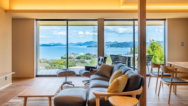 A modern living room with a large window offering a scenic view of the sea and mountains. - Setouchi golf resort Villa (Takehara)