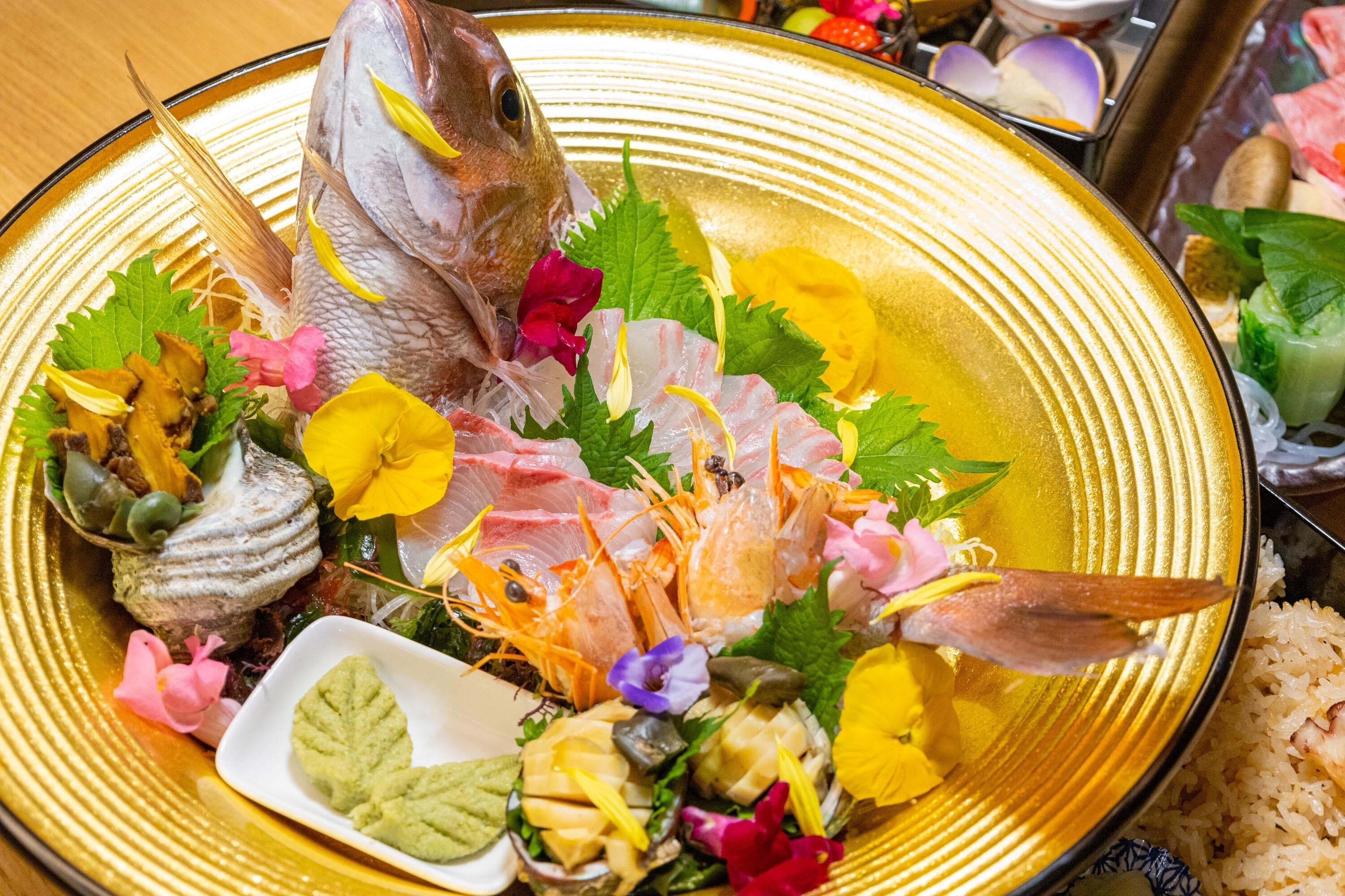 A seafood platter with various types of fish and shellfish, garnished with herbs and flowers.