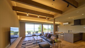 A spacious living area with a large window, a sofa, a coffee table, and a kitchen area with a countertop and sink. - Setouchi golf resort Villa (Takehara)
