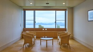 A room with a large window, two wicker chairs, a small round table, and a wooden floor. - Setouchi golf resort Villa (Takehara)