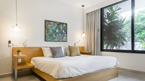 A modern bedroom with a wooden bed, a side table, a wall-mounted painting, and a large window with curtains. - Opal Suites (Playa del Carmen)