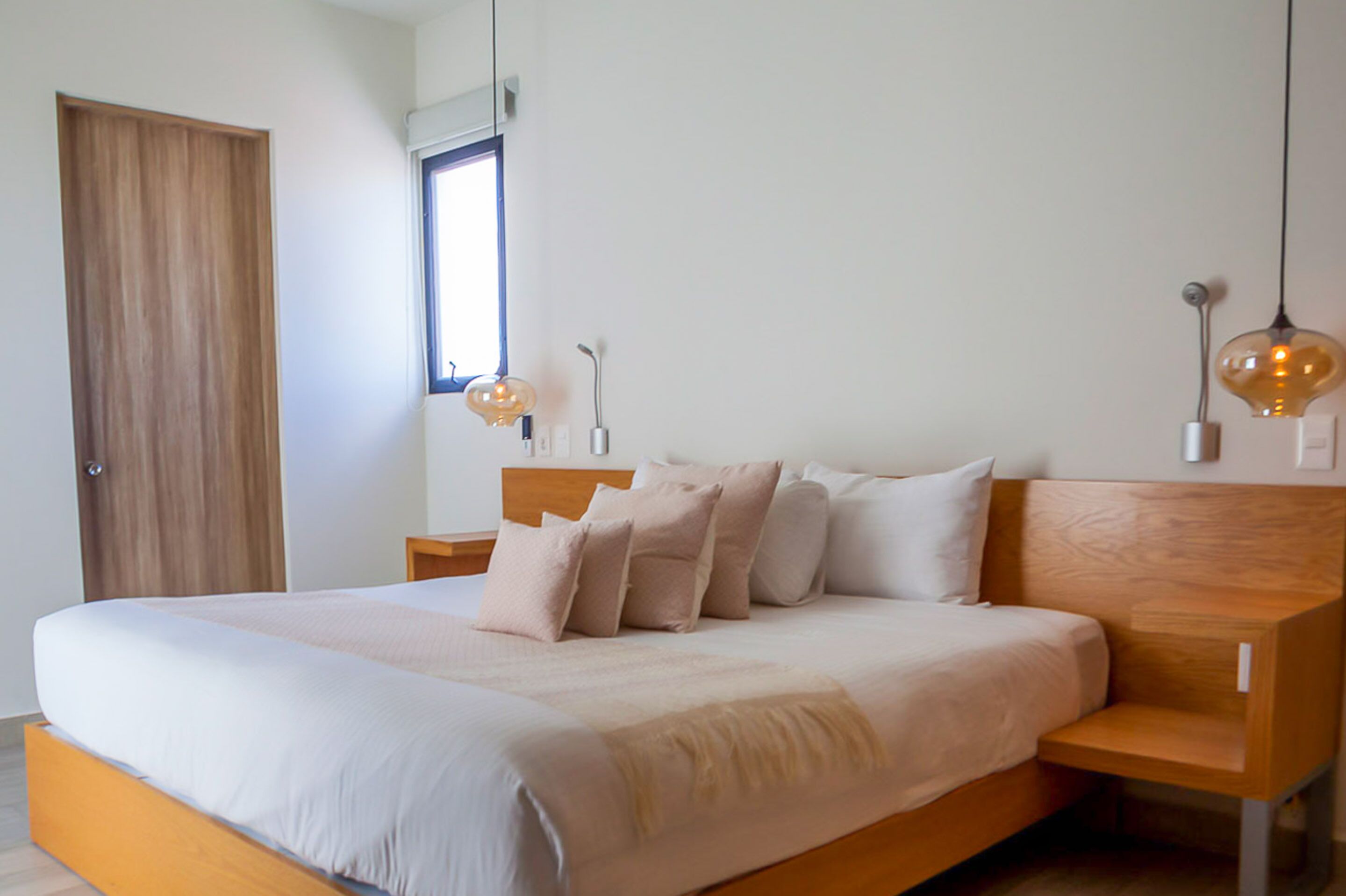 Quarto moderno com estrutura de cama de madeira, uma janela grande e duas luminárias pendentes.