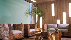 A modern living room with a wooden wall, a large plant, and a sofa set. - Opal Suites (Playa del Carmen)