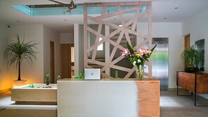 A modern reception desk with a laptop, surrounded by plants and a decorative wall. - Opal Suites (Playa del Carmen)