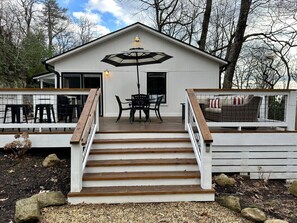 Una casa a due piani con una veranda in legno, un tavolo da pranzo con sedie e una scala che conduce al piano superiore.
