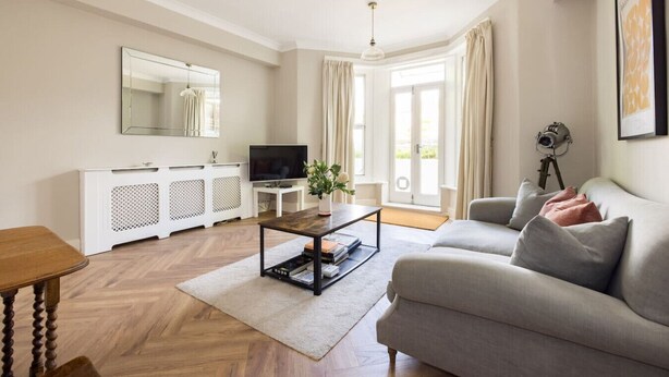 A living room with a sofa, TV, white cabinet, and a large window with curtains.