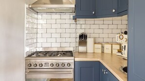 A kitchen with a stainless steel stove, white tiled backsplash, blue cabinets, and a coffee machine.