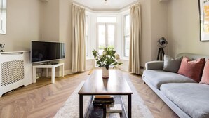 A living room with a television, sofa, coffee table, and a window with curtains.