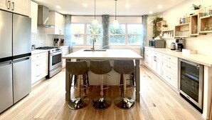 Une cuisine moderne dotée d’un îlot central, de tabourets de bar, d’appareils électroménagers en acier inoxydable et d’une grande fenêtre qui laisse entrer la lumière naturelle.
