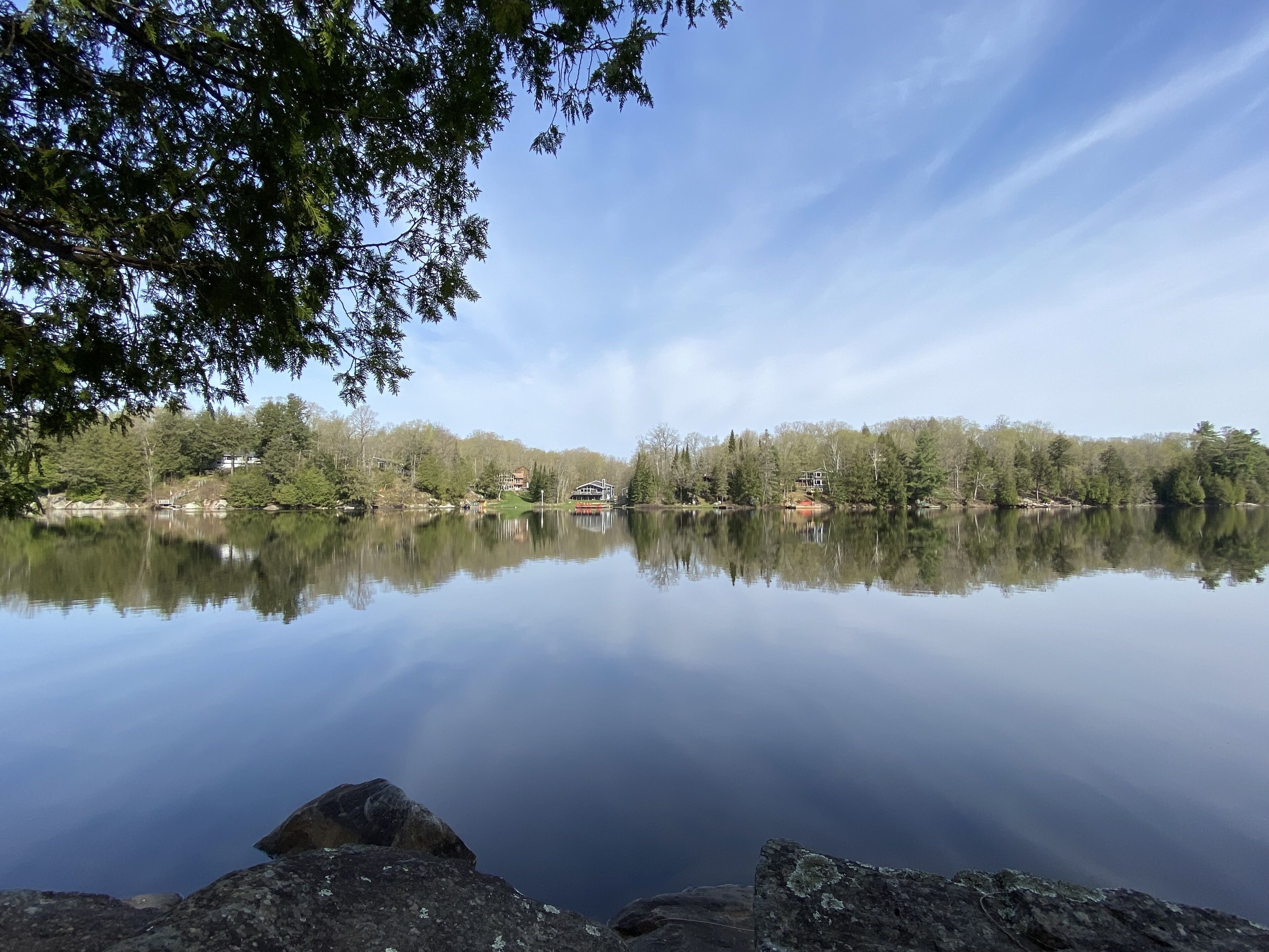 Un lac paisible où se reflètent les arbres et les bâtiments, entouré d’une forêt.