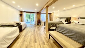 Une chambre avec deux lits, un banc, un plancher en bois et une vue sur les arbres par la porte.