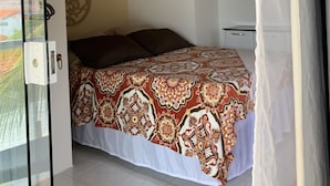 A bedroom with a patterned bedspread, a ceiling fan, and a view of the outside. - Casa D'Jhú (Vera Cruz)
