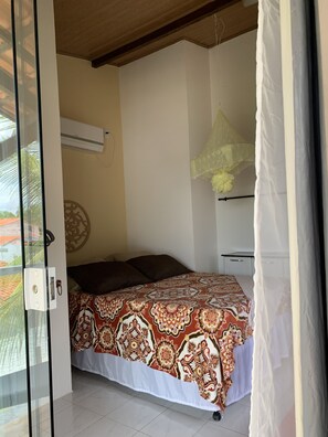 Quarto com colcha estampada, ventilador de teto e vista para o exterior.