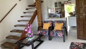 A staircase with wooden steps and a brick pillar, a sofa with floral upholstery and yellow cushions, and a small table with a vase of flowers. - Casa D'Jhú (Vera Cruz)