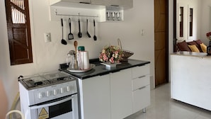 A kitchen with white cabinets, a stove, a sink, and a countertop with various kitchen utensils and a vase of flowers. - Casa D'Jhú (Vera Cruz)