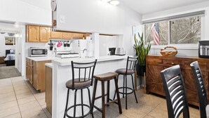 A modern kitchen with white cabinets, a central island with stools, a stove, microwave, and refrigerator.