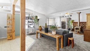 A spacious living room with a large wooden table, grey sofa, and a stone fireplace.